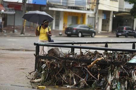 Mulher de guarda-chuva observa lixo acumulado nas pontes do Rio Maracanã, na Tijuca