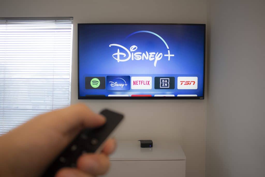 Pessoa segurando controle remoto e apontando para televisão com a plataforma de streaming Disney+ em destque