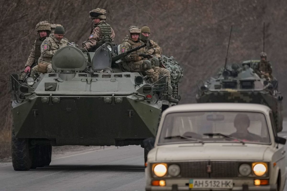 Ukrainian service members sit atop armored vehicles driving in eastern Ukraine