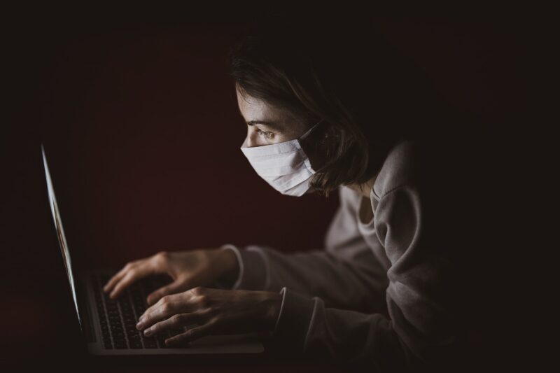 cérebro pandêmico (imagem mostra mulher de máscara usando notebook no escuro)