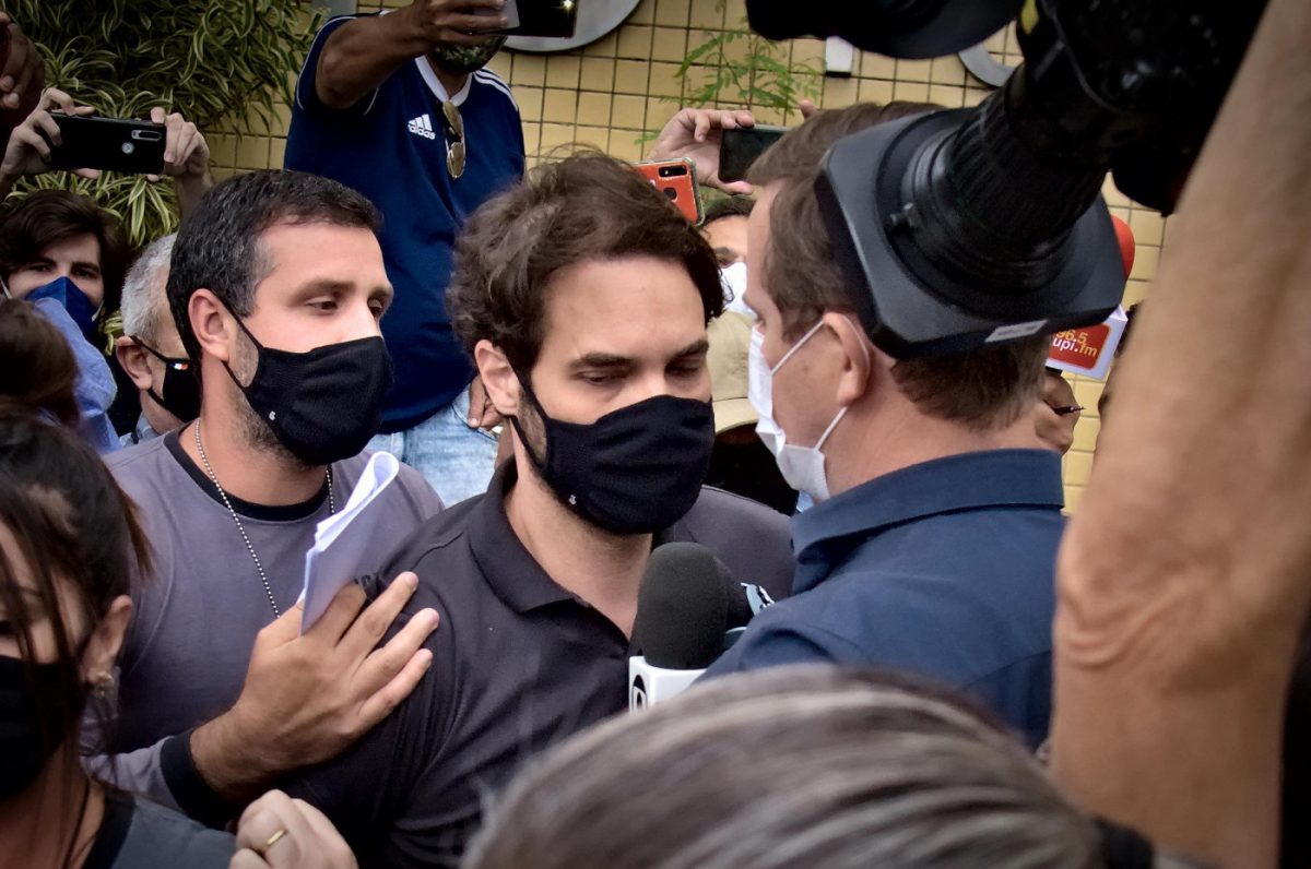 Jairinho, que assassinou o menino Henry Borel, com uma multidão em volta. Ele usa camisa polo preta e máscara de proteção.