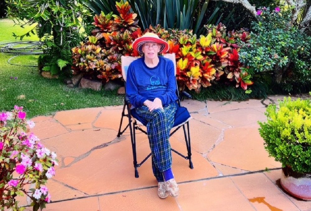Rita Lee sentada em cadeira em meio a jardim