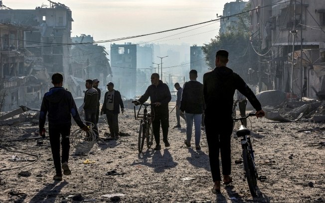 Homens caminham sobre os escombros perto de um prédio residencial na rua Jalaa bombardeado por Israel, em 14 de janeiro de 2025 na Cidade de Gaza