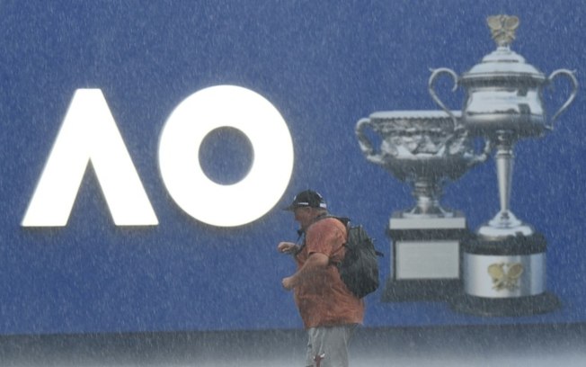 Um homem caminha sob forte chuva no primeiro dia do Aberto da Austrália.