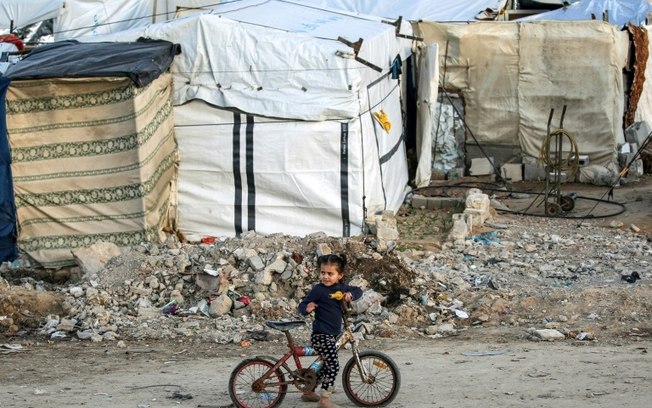 Uma menina anda de bicicleta em frente a um acampamento para pessoas deslocadas pelo conflito em Bureij, centro da Faixa de Gaza, em 17 de janeiro de 2025 Uma menina anda de bicicleta em frente a um acampamento para pessoas deslocadas pelo conflito em Bureij, centro da Faixa de Gaza, em 17 de janeiro de 2025