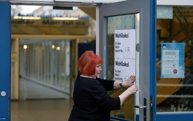 Funcionária eleitoral cola cartaz na entrada de centro de votação em Berlim