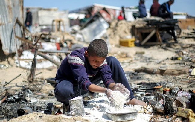 Um menino coleta farinha após um suposto bombardeio israelense contra uma tenda para deslocados em Khan Yunis, sul da Faixa de Gaza, em 17 de abril de 2025