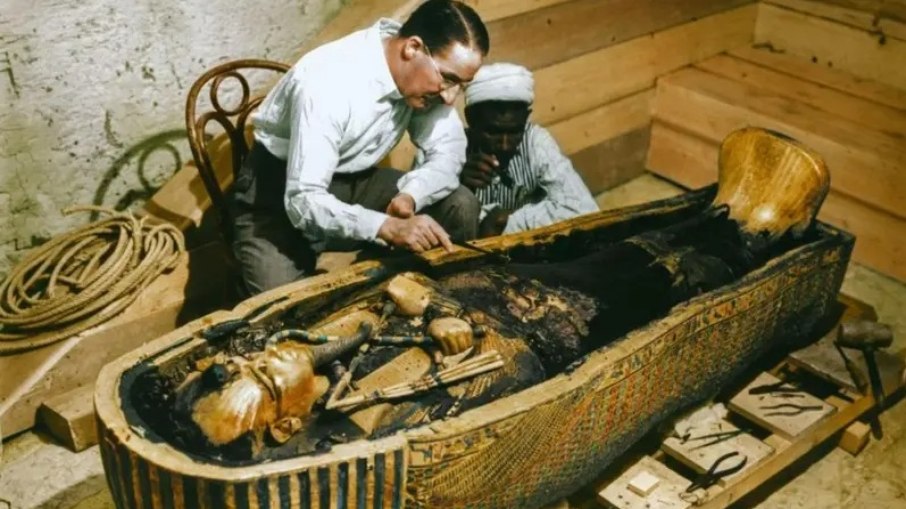 Arqueólogo britânico Howard Carter e um trabalhador egípcio examinam um caixão feito de ouro maciço dentro da tumba Arqueólogo britânico Howard Carter e um trabalhador egípcio examinam um caixão feito de ouro maciço dentro da tumba