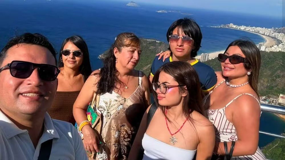 Seis turistas sorrindo em ponto turístico com vista do mar e cidade do Rio